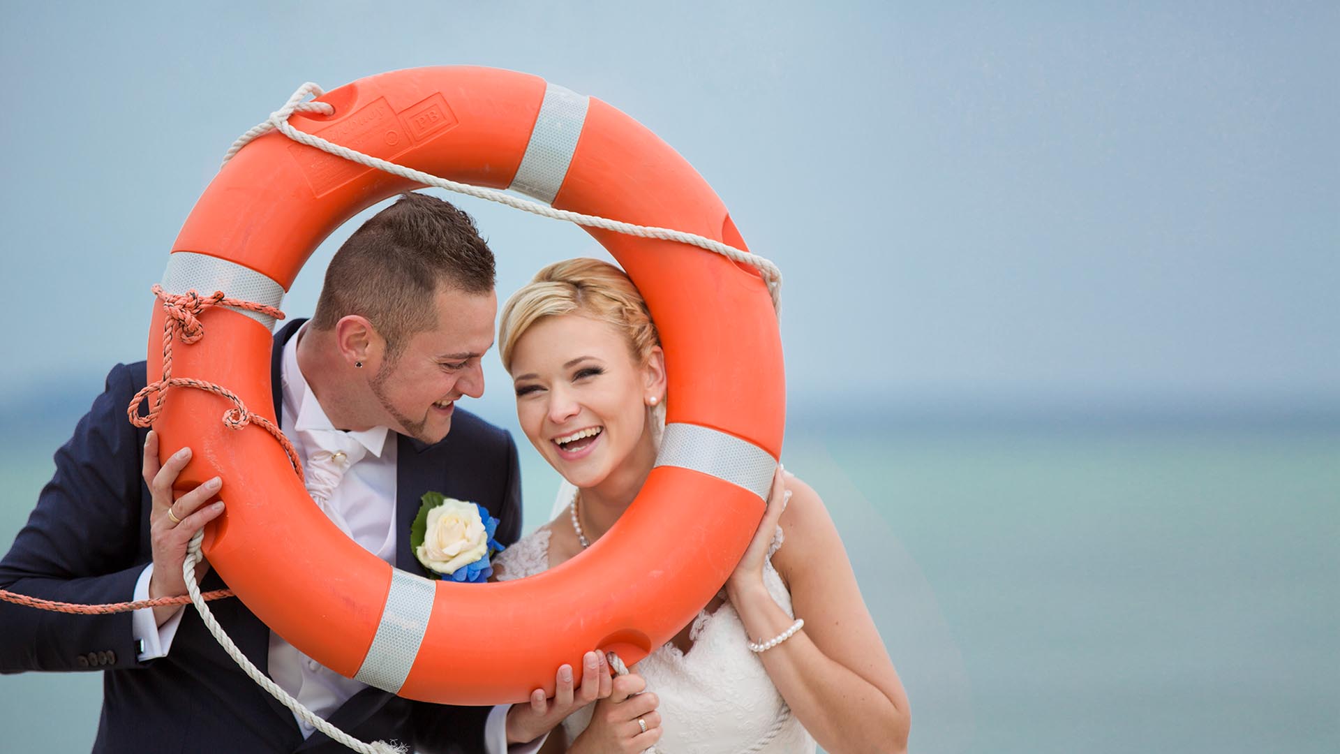 Portrait vom lachenden Brautpaar am Ostsee mit Rettungsring